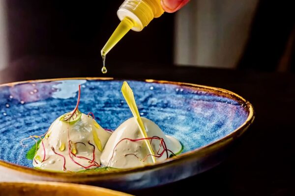 Alchimia gustului Chef Silviu adaugă cu pipeta o picătură de ulei peste un preparat cremă servit într-un bol albastru cu accente aurii
