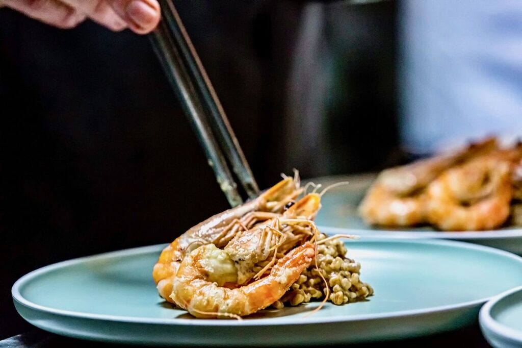 Armonia detaliului Chef Silviu așază cu penseta creveți caramelizați pe un pat de cereale, într-un plating rafinat.