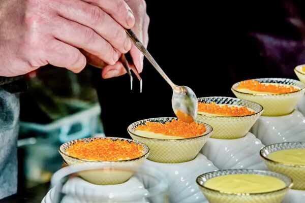 Precizia perlei Chef Silviu așază icre portocalii de somon peste o cremă fină, folosind lingura și penseta pentru detalii precise.