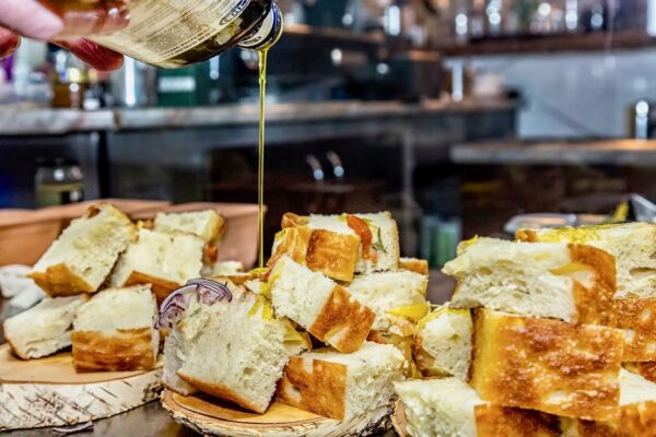 Focaccia cu ierburi mediteraneene Focaccia reinterpretată, stropită cu ulei de măsline BIO presat la rece, servită rustic pe suport de lemn.