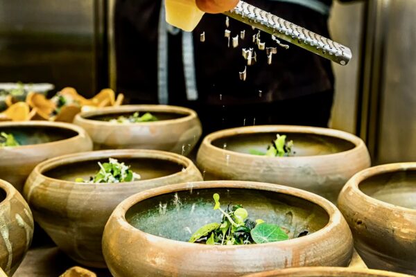 Ritualul gustului Chef Silviu adaugă ingrediente proaspete peste preparate în boluri ceramice, în timpul unui plating rafinat.