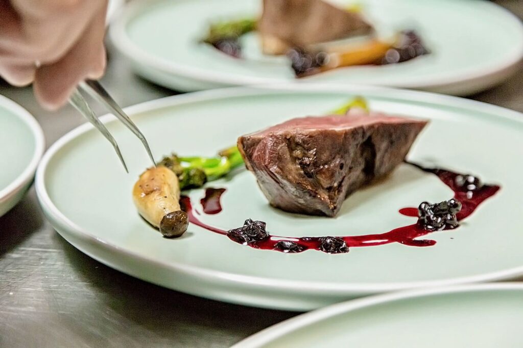 Plating precis – echilibru și rafinament Silviu Atanasie realizează platingul unei farfurii cu carne roșie, legume caramelizate și sos de fructe de pădure în cadrul atelierului culinar.